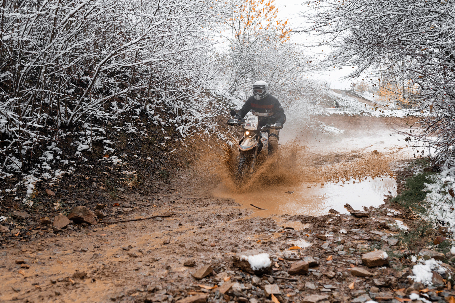 Ein Foto einer Person trägt eine Rally Raid Jacke von Fuel Motorcycle und fährt eine BMW HP2 durch eine Pfütze. Hochwertige Fotografie von JNPhotografics